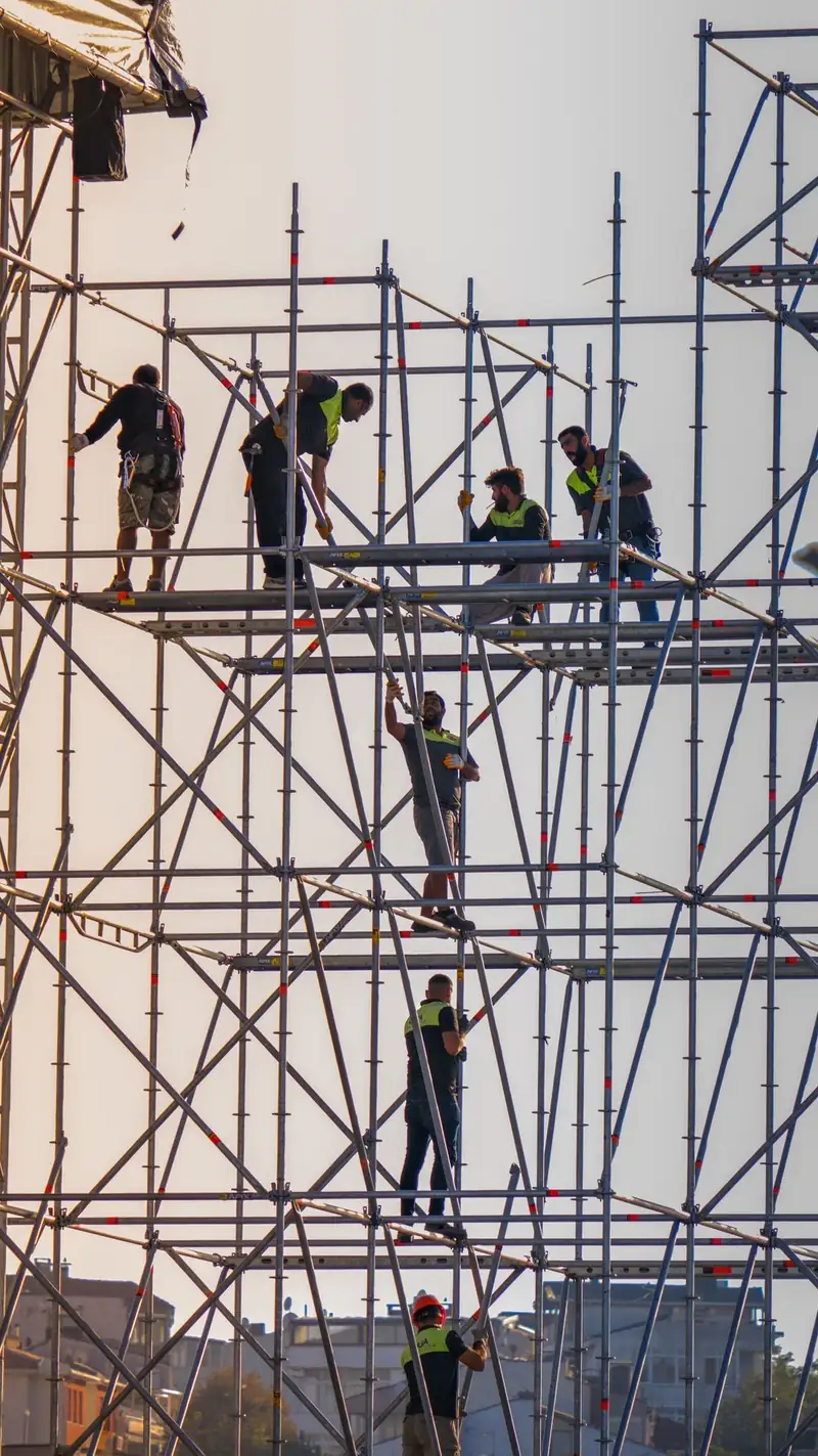Workers erecting galvanized steel ringlock scaffolding on a construction site